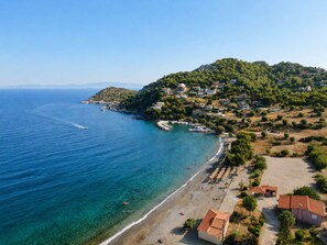 Vue aérienne d’une ville côtière avec une plage, une mer d’un bleu limpide et des maisons situées sur les flancs d’une colline.
