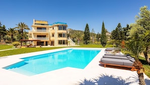 Una casa de dos pisos con piscina, mobiliario de exterior y un jardín bien cuidado.