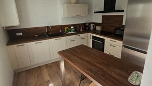 A modern kitchen with white cabinets, a wooden countertop, a stainless steel refrigerator, and a hanging light fixture. - Maison avec jardin suspendu - vue sur le Donjon (Loches)