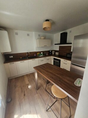 Eine moderne Küche mit weißen Schränken, einer Holz Arbeitsplatte, einem Edelstahlkühlschrank und einer Pendelleuchte.