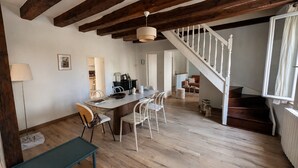 A dining area with a wooden table, white chairs, a lamp, and a staircase leading to another room. - Maison avec jardin suspendu - vue sur le Donjon (Loches)