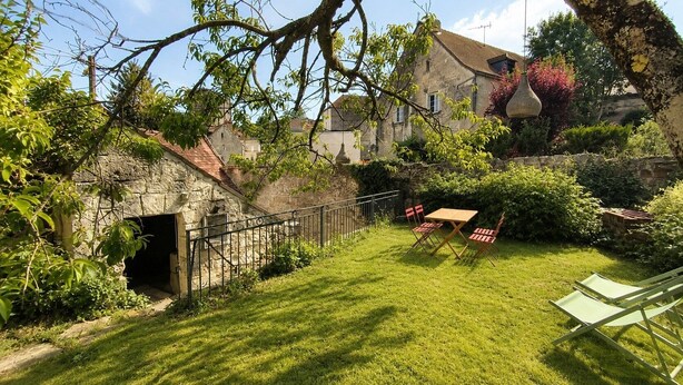 A stone building with a small garden, a wooden table with chairs, and a metal fence. - Maison avec jardin suspendu - vue sur le Donjon (Loches)
