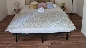 A bedroom with a sloped ceiling, a bed with a woven headboard, a bedside table with a lamp, and a floor lamp. - Maison avec jardin suspendu - vue sur le Donjon (Loches)