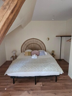 Ein Schlafzimmer mit schrägen Wänden, einem Bett mit gewobener Kopfteil, einem Nachttisch mit Lampe und einer Stehlampe.