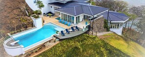 A modern house with a swimming pool, outdoor seating, and a view of the surrounding landscape.