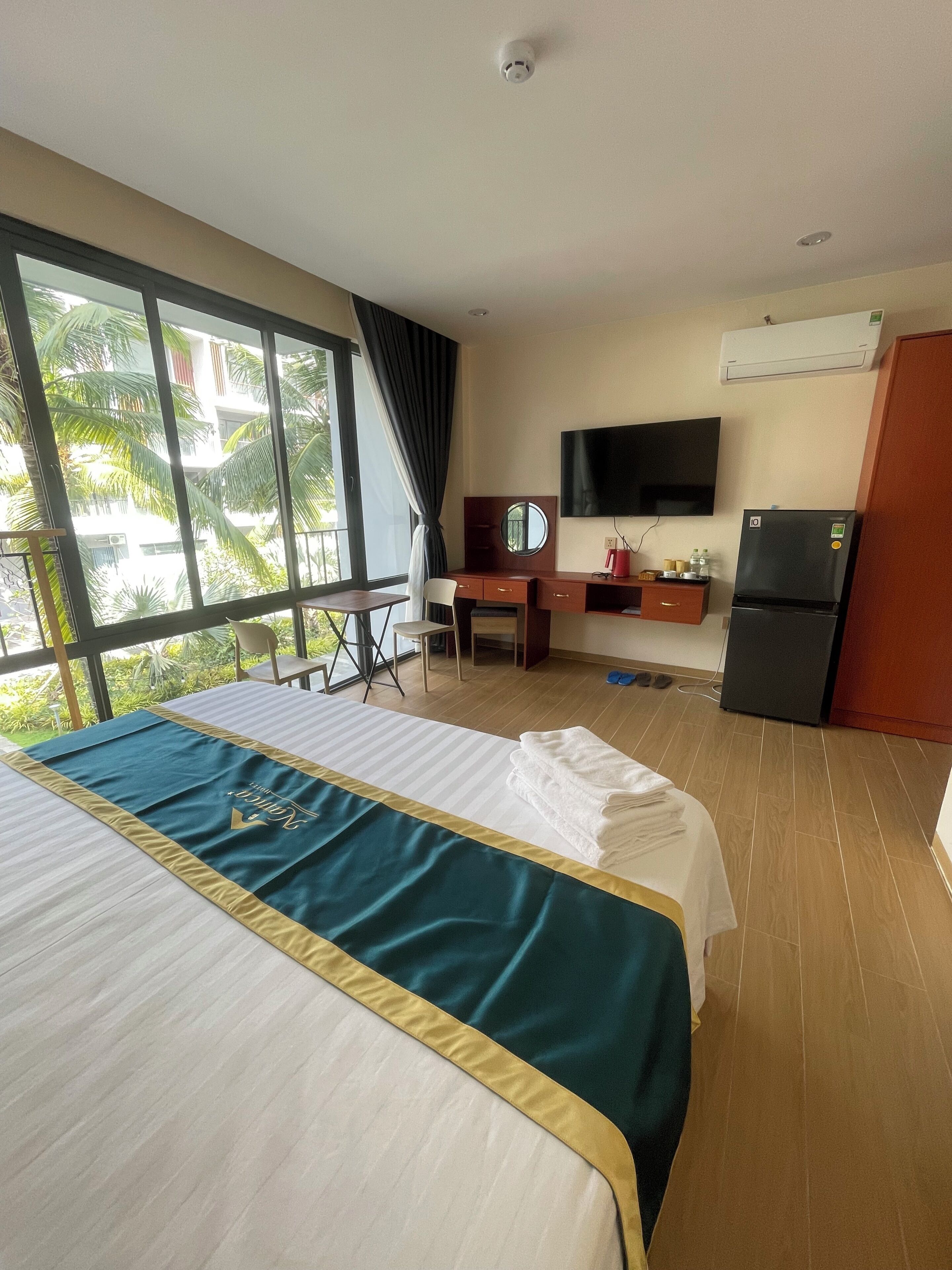 A hotel room with a bed, desk, chair, TV, and a refrigerator.
