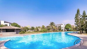A swimming pool with a curved edge, surrounded by a tiled deck and a few trees. - Namca Hotel  (Phu Quoc)