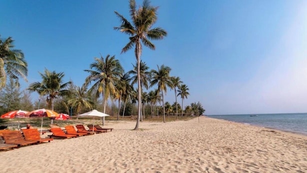 A beach with rows of wooden lounge chairs and umbrellas, palm trees, and a clear sky. - Namca Hotel  (Phu Quoc)