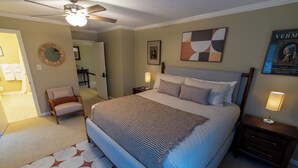 A bedroom with a large bed, a chair, a bedside table, a lamp, a ceiling fan, and a framed picture on the wall. - The Cunningham (Salina)