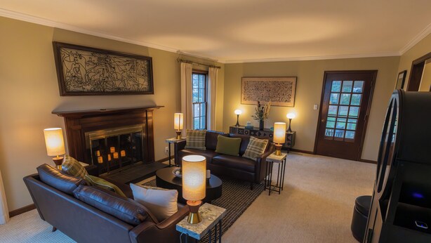 A living room with a fireplace, sofas, lamps, and a large abstract painting on the wall. - The Cunningham (Salina)