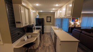 A compact kitchen with white cabinets, a black refrigerator, and a wooden floor. - The Cunningham (Salina)