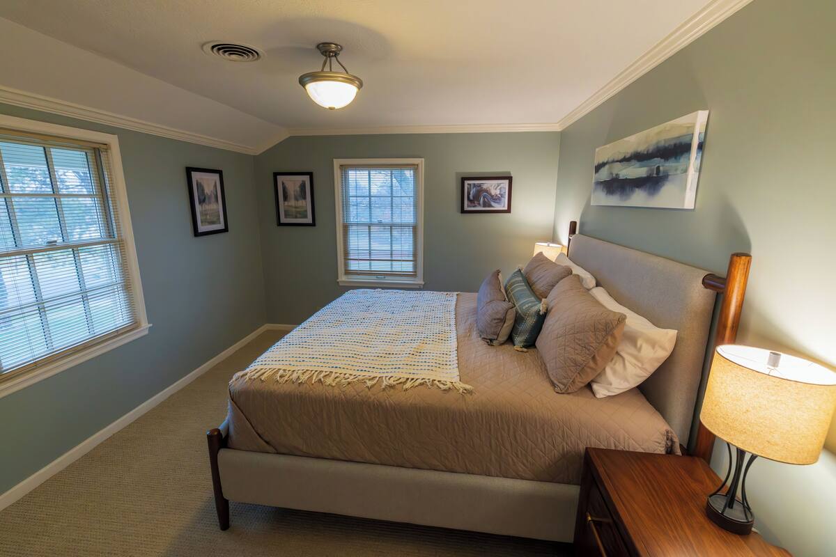 A bedroom with a bed, two windows, a ceiling fan, and a wall-mounted lamp.