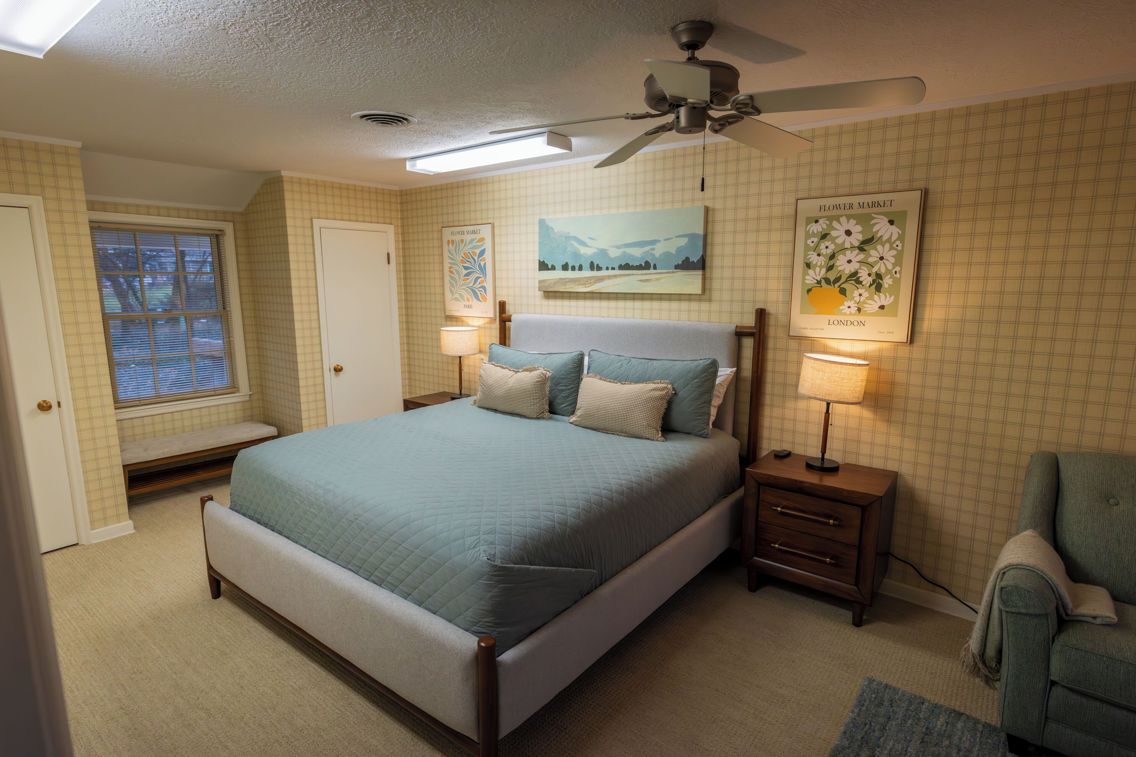 A bedroom with a bed, bedside tables, a chair, a ceiling fan, and a window with blinds.