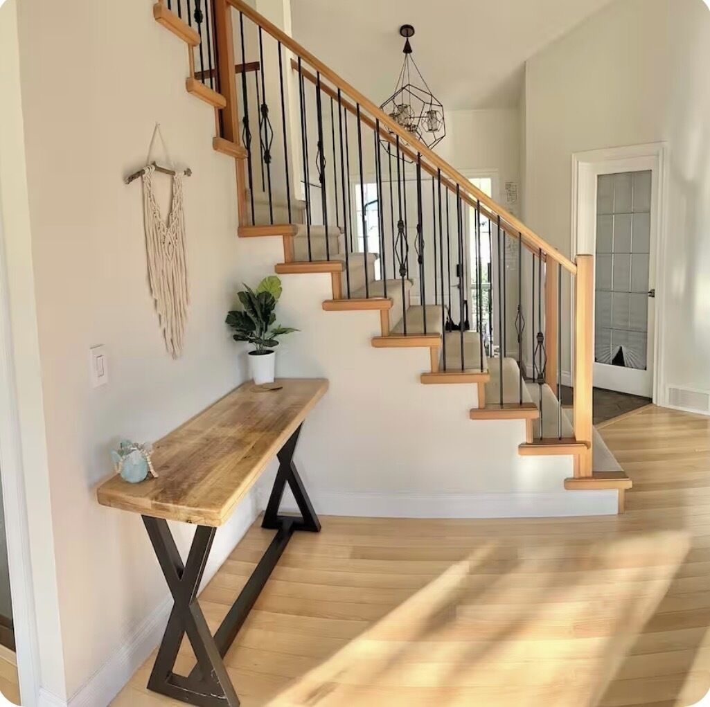 Un escalier avec des marches en bois et des rampes en métal, un banc en bois, une plante en pot et une décoration murale en macramé.