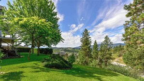 Une pelouse bien entretenue, avec un grand arbre, un petit arbuste et, au loin, une vue sur un quartier résidentiel.