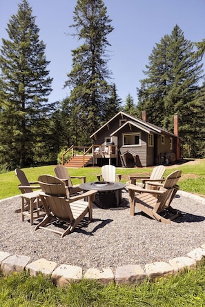 A lodge with a deck, a fire pit, and Adirondack chairs.
