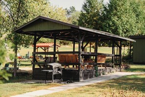 Un espace extérieur abrité, aménagé avec un barbecue, des chaises en bois et une table.
