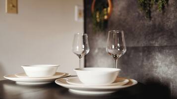 Una mesa de comedor con cuencos blancos y copas de vino, una mesa de madera oscura, y una pared con un adorno de guirnalda.