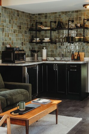 Una cocina moderna con salpicadero de azulejos, armarios negros, una cafetera y un comedor con mesa y sillas.