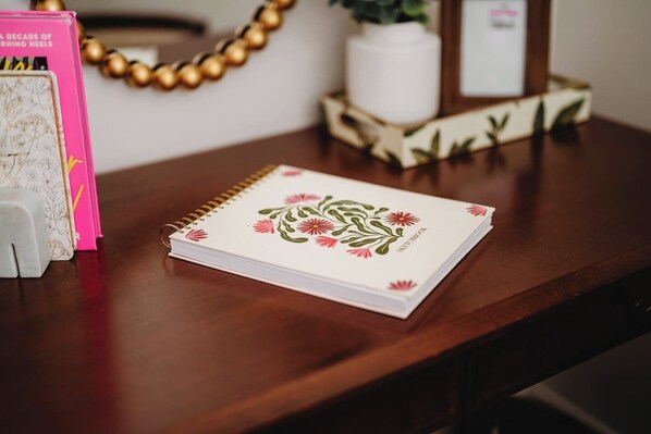 A notebook on a wooden table with a floral design, surrounded by a decorative vase, a plant, and a framed picture. - Farmhouse 18ppl at Casacampo (Wisconsin Dells)