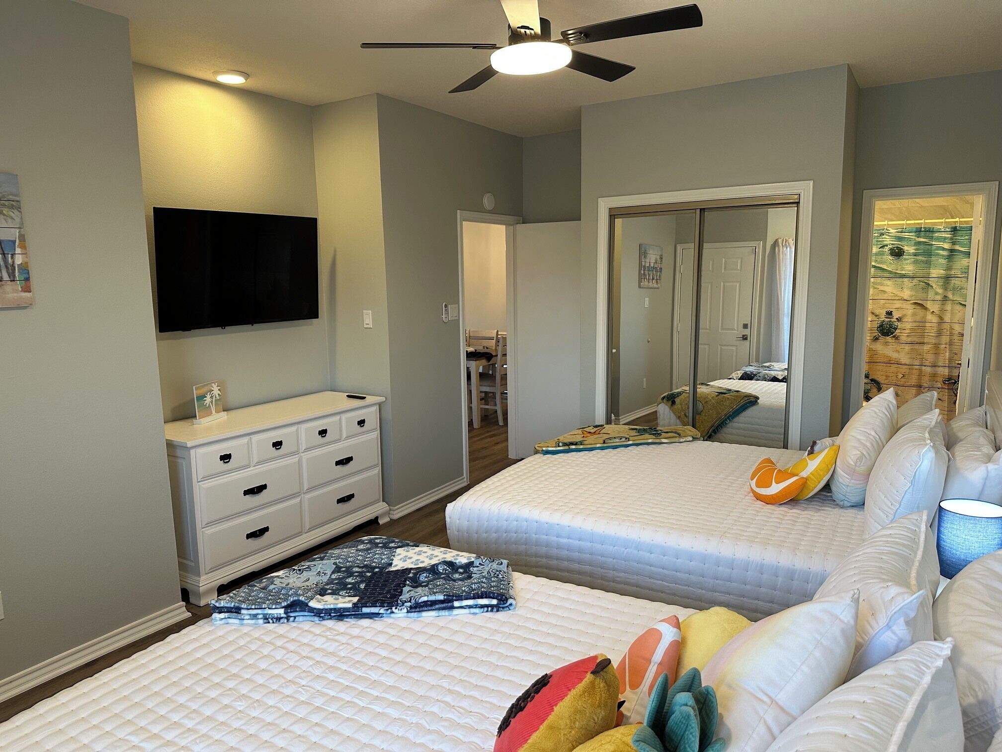 A bedroom with two beds, a dresser, a ceiling fan, and a television.
