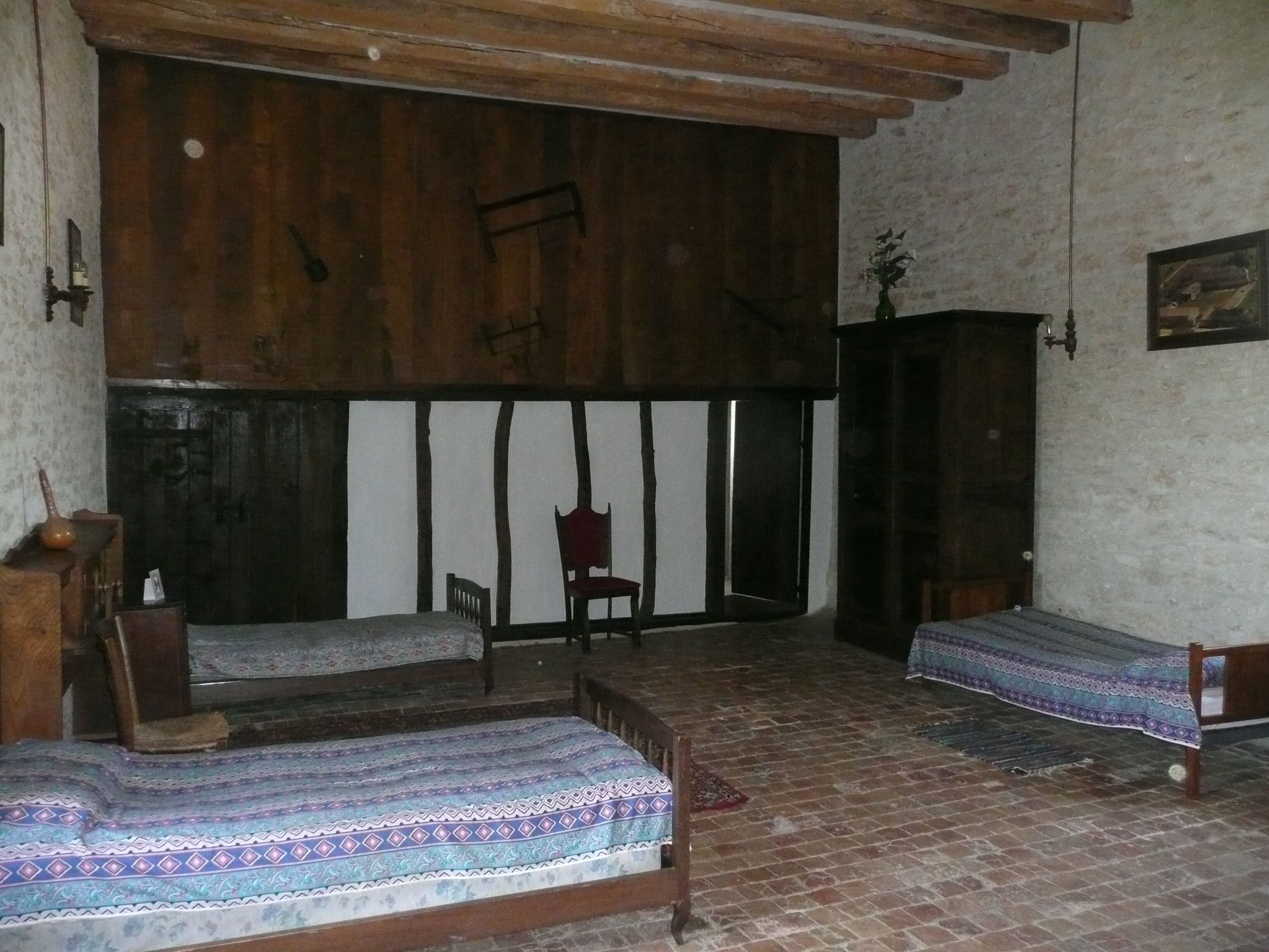 Una camera rustica con travi in legno al soffitto, un letto con copriletto decorato, una sedia e un piccolo tavolo con un vaso.