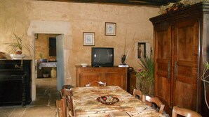 Een eethoek met een tafel voor vier personen, een televisie op een houten kast, en een deur naar een andere kamer.