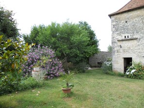 Ein Innenhof mit einem Steinhaus, üppigem Grün und einem blühenden Strauch.