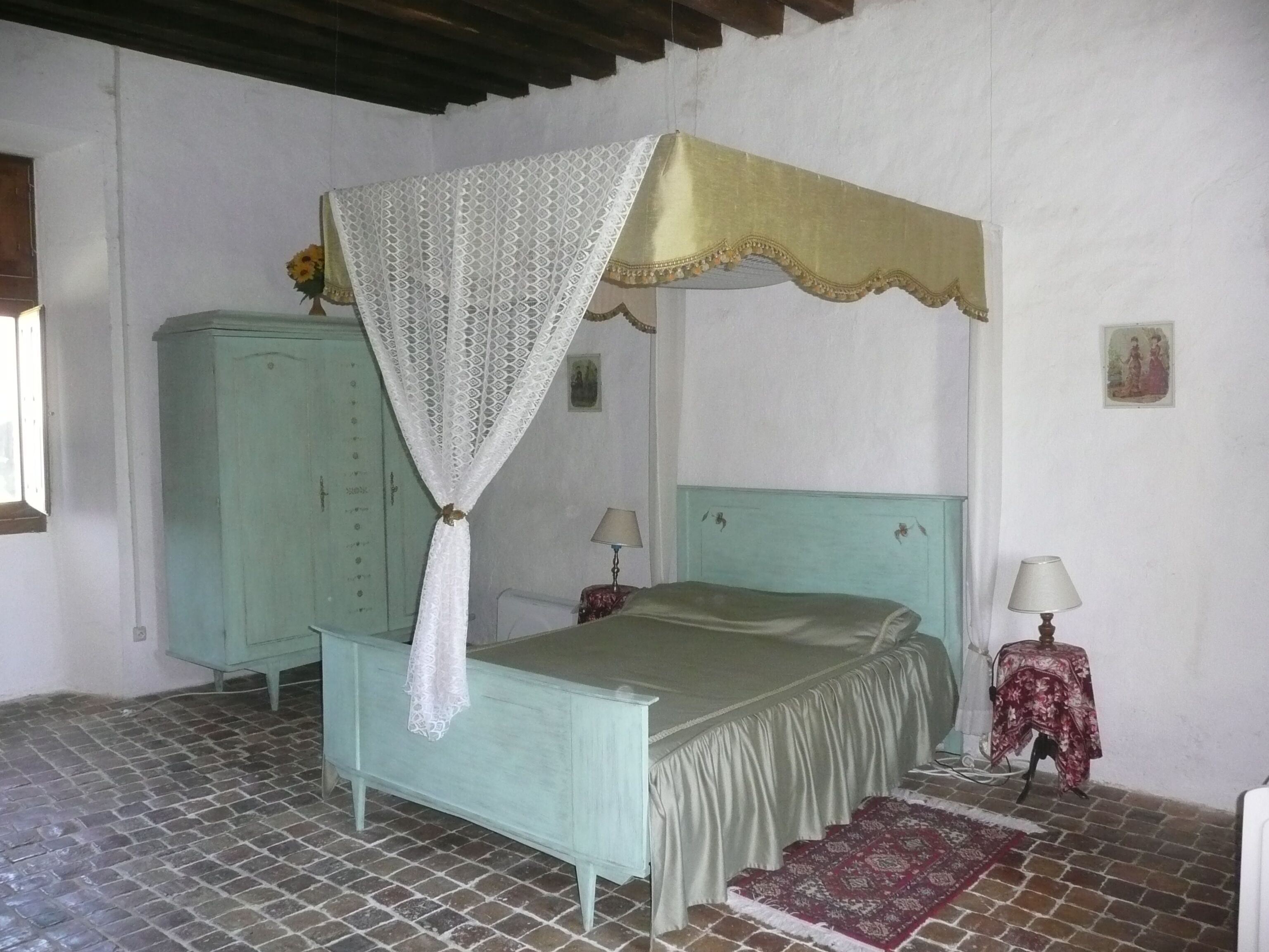 Une chambre avec un lit, une armoire, une table avec une lampe et un tapis à motifs.