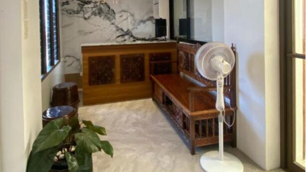 Quarto com teto de madeira, parede de mármore, um banco de madeira, um ventilador e um vaso com planta.