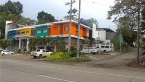 Um edifício de vários andares com um espaço comercial no andar térreo, incluindo uma loja 7-Eleven. Há veículos estacionados na rua em frente.