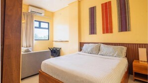 Quarto de hotel com uma cama, um sofá, um ar condicionado, uma janela e duas obras de arte penduradas na parede.