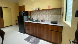 Cozinha compacta com armários de madeira, uma geladeira preta, micro-ondas e pia.