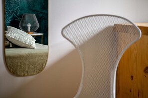 A room with a bed, a round mirror, and a white mesh chair.