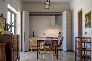 A modern kitchen with a dining area, featuring a table with chairs, a pendant light, and a view to the outside.
