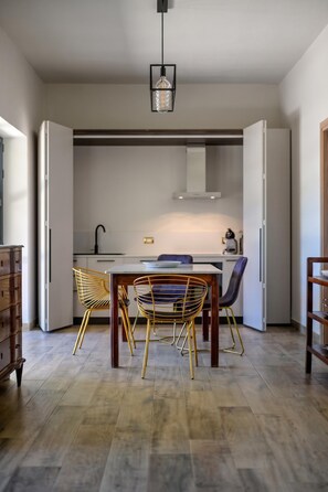 A modern kitchen with a dining area, featuring a wooden table, two chairs, and a hanging light fixture.