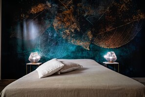 A bed with two bedside lamps, a textured wall, and a leaf-patterned mural.
