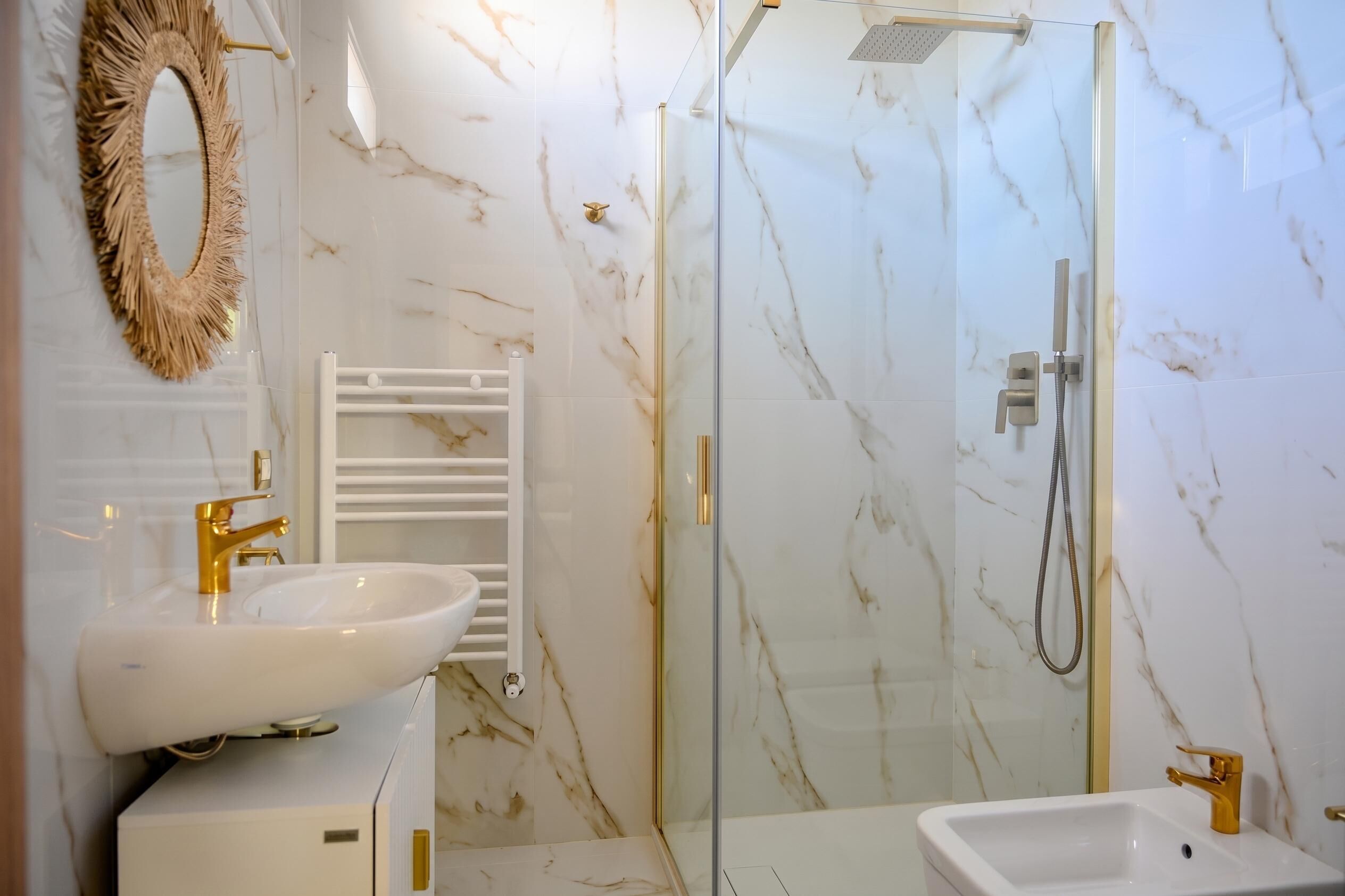 A bathroom with a white sink, gold faucets, a glass-enclosed shower, and marble walls.