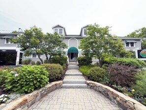 A two-story building with a central entrance, a covered porch, and a landscaped garden with a stone pathway leading to the entrance. - Ogunquit Studio 2-Min Walk to Downtown (Ogunquit)