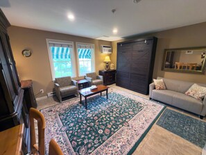 A living room with a sofa, armchairs, a coffee table, a patterned rug, and a large dark door.