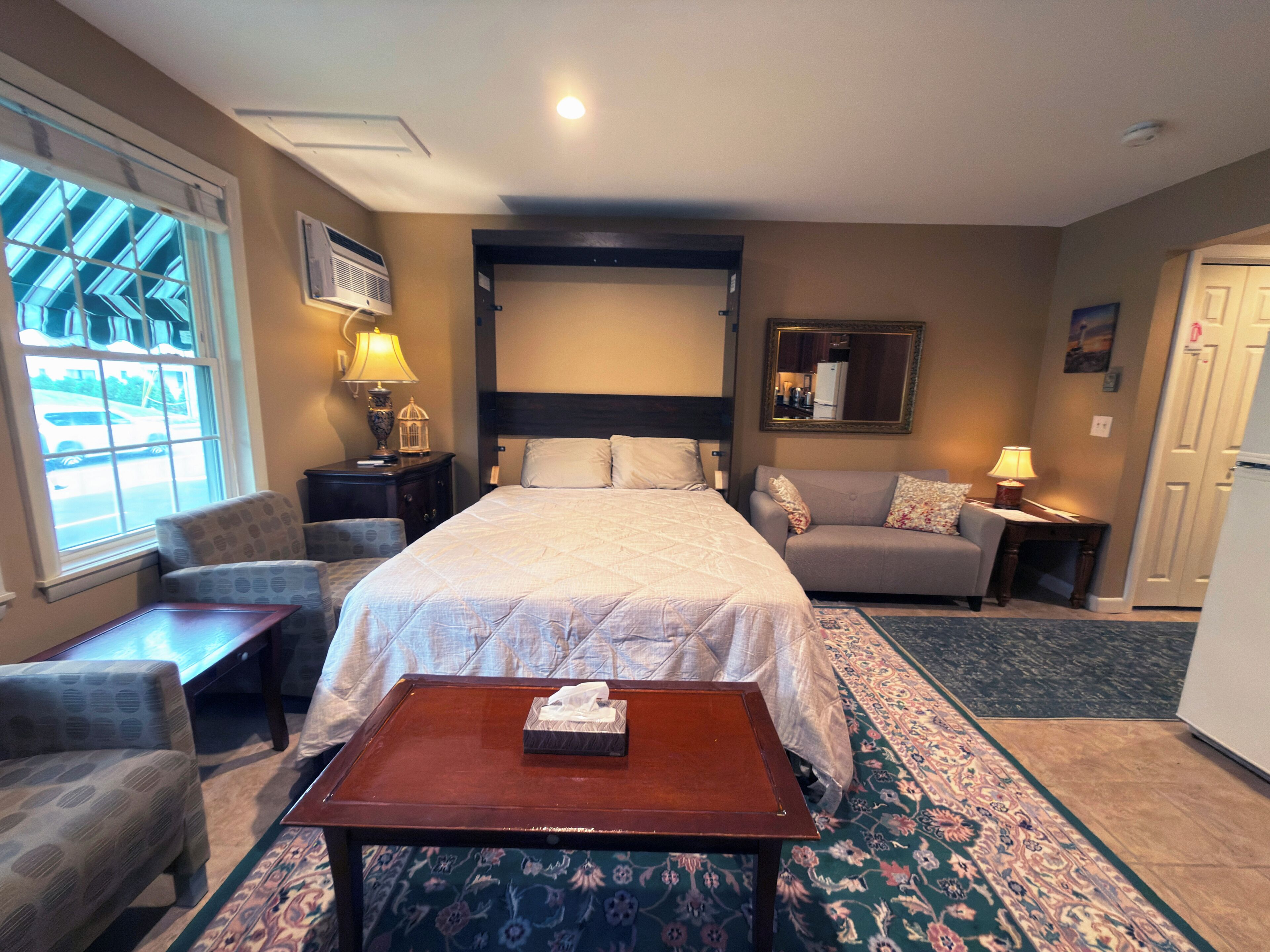 Une chambre d’hôtel avec un lit, un canapé, une petite table, une lampe, un miroir et une fenêtre donnant sur l’extérieur.