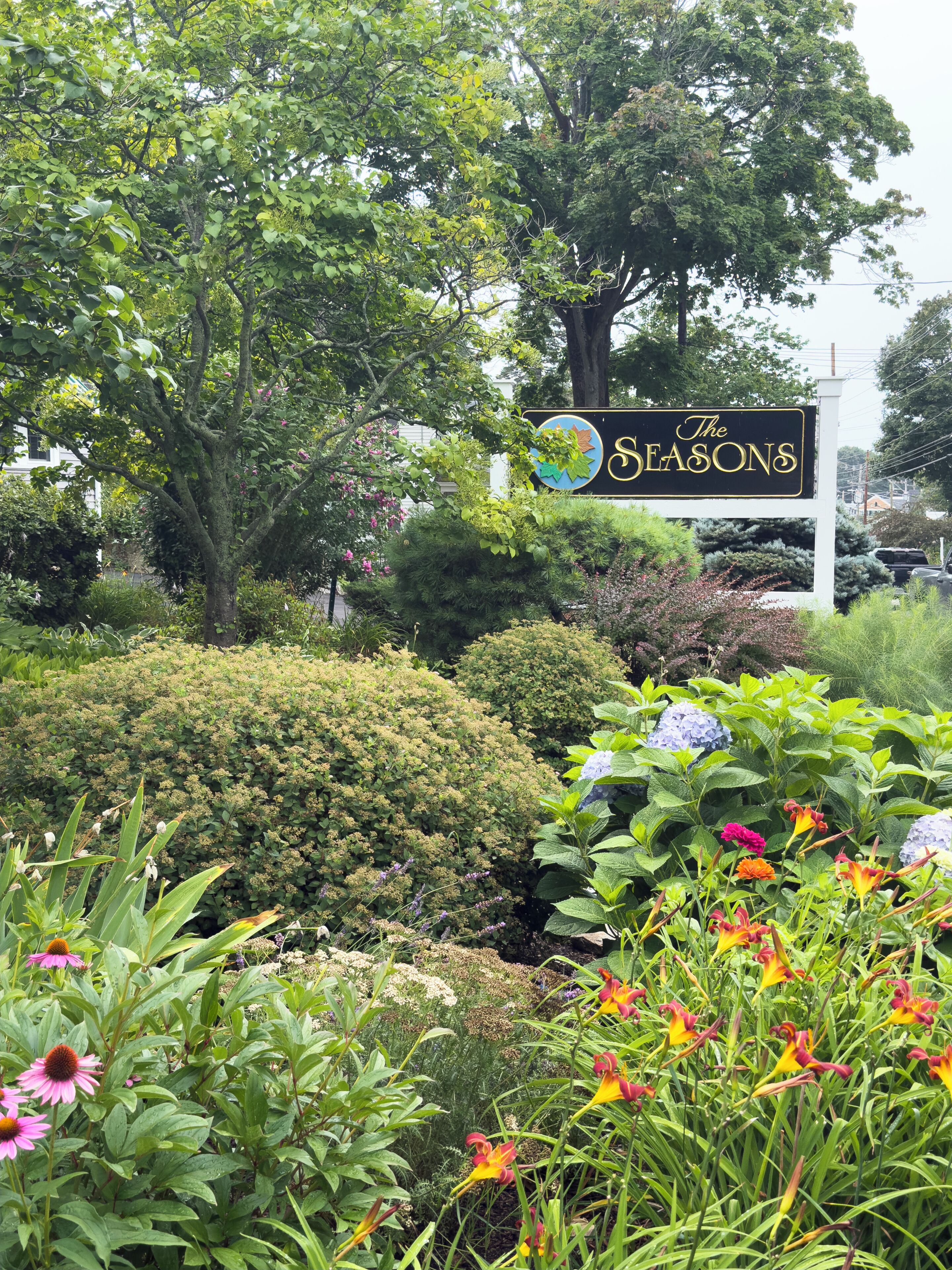 A sign for 'The Seasons' hotel surrounded by lush greenery and flowering plants.