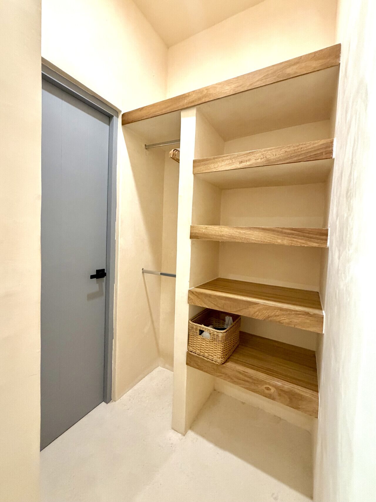 A hallway with a door, a wooden shelf unit with baskets, and a towel rack.