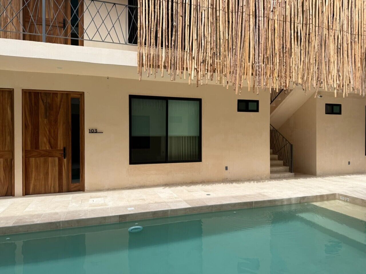 A modern building with a swimming pool, wooden doors, and a staircase.