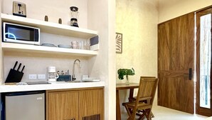 Une cuisine compacte équipée d’un four à micro-ondes, d’une machine à café et d’un petit réfrigérateur. Un coin repas est aménagé avec une table et des chaises en bois.