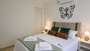 Ein Hotelzimmer mit einem Bett, zwei Kissen, einem Nachttisch mit Lampe und einer Wand-Klimaanlage.