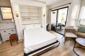 Ein Schlafzimmer mit Bett, Nachttisch, Sessel, Sofa, Schreibtisch und einer Schiebetür zum Balkon.