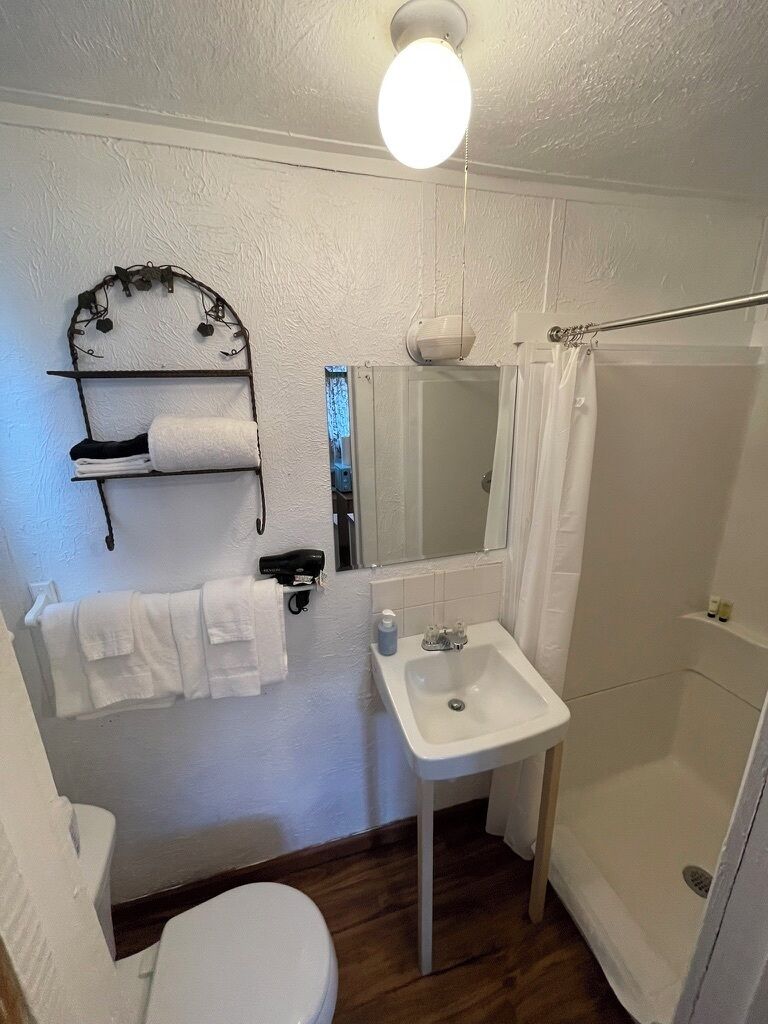 Casa de banho com sanita, lavatório, chuveiro e porta-toalhas.