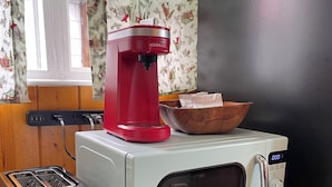 A kitchenette with a toaster, a red coffee maker, a microwave, and a wooden cabinet. - Lone Pine Cabins  (Grand Lake)
