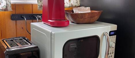 A kitchenette with a toaster, a red coffee maker, a microwave, and a wooden cabinet.